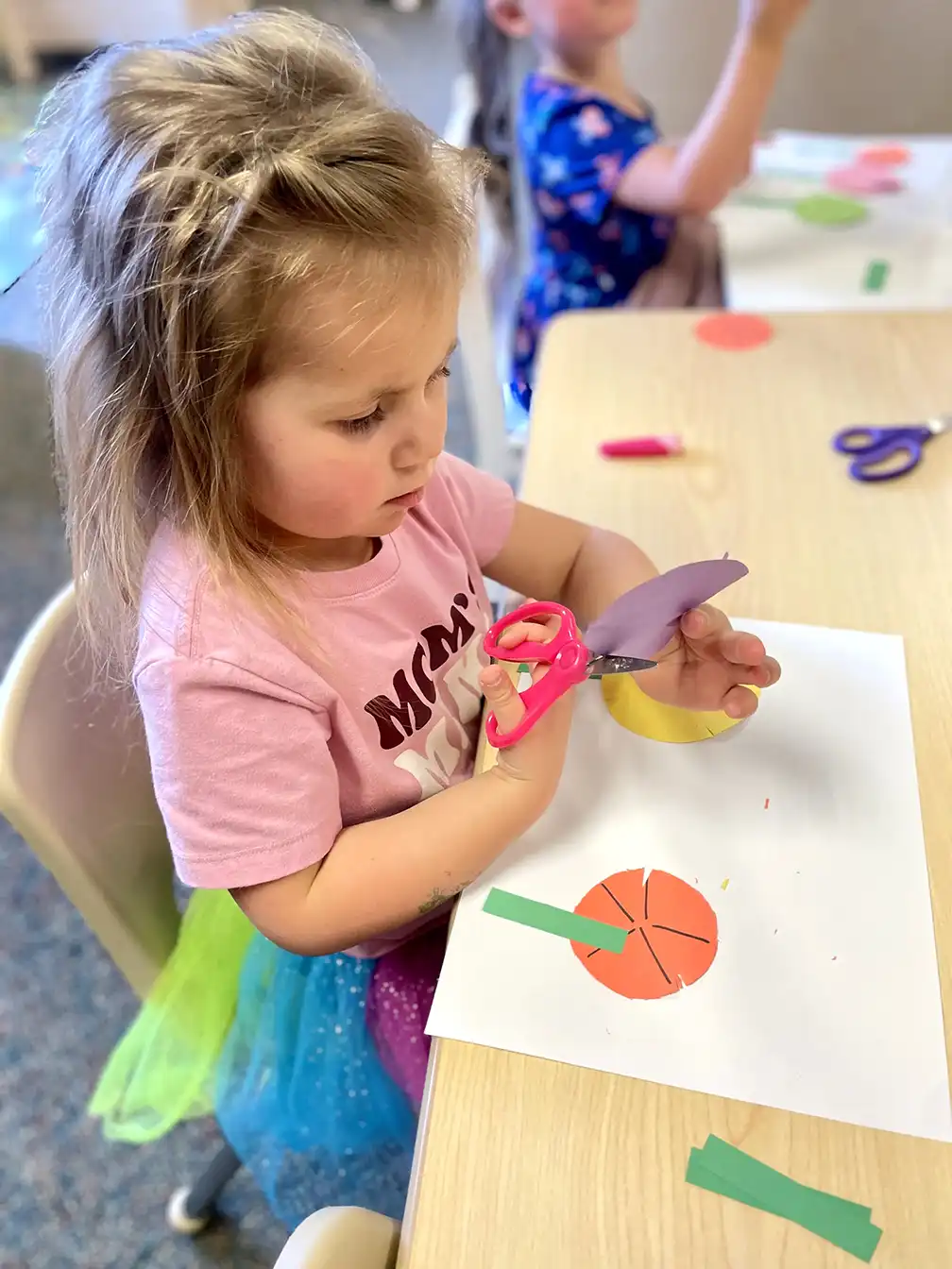 Growing Roots Early Learning student cutting construction paper shapes with scissors.